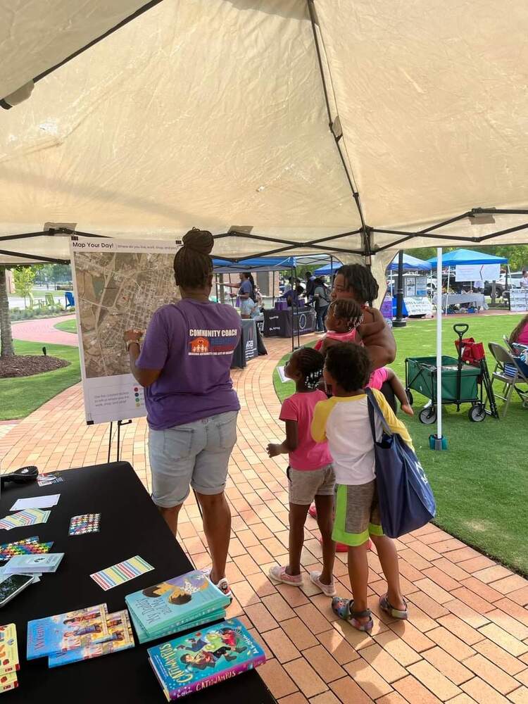 A family engaging with staff member in front of vendor table with books and blueprint