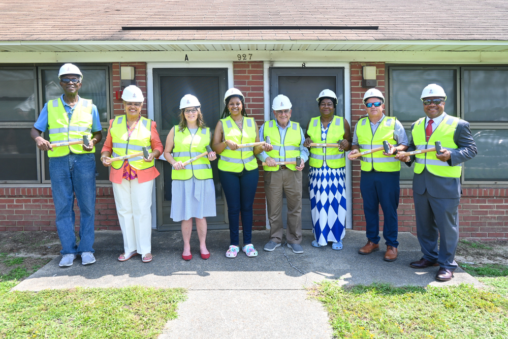 Fairview renovation participants wearing hard hats with hammers in hand outside Fairview unit