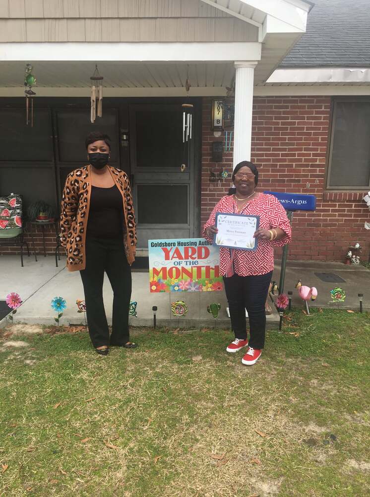 Mercy Freeman outside her residence holding a Yard of the Month certificate with a HACG Staff member